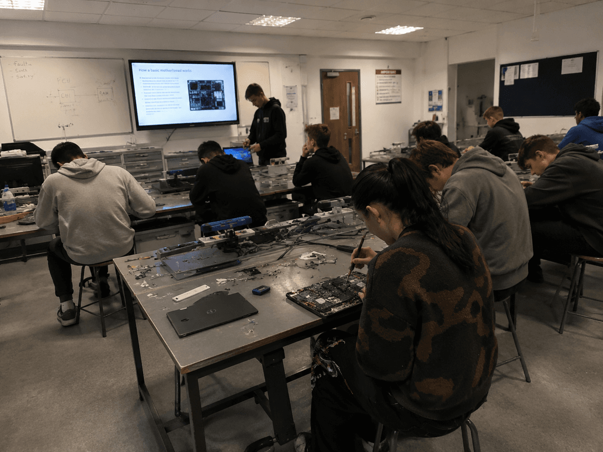 A college computing classroom, students working on stripped down laptops and motherboards at metal benches