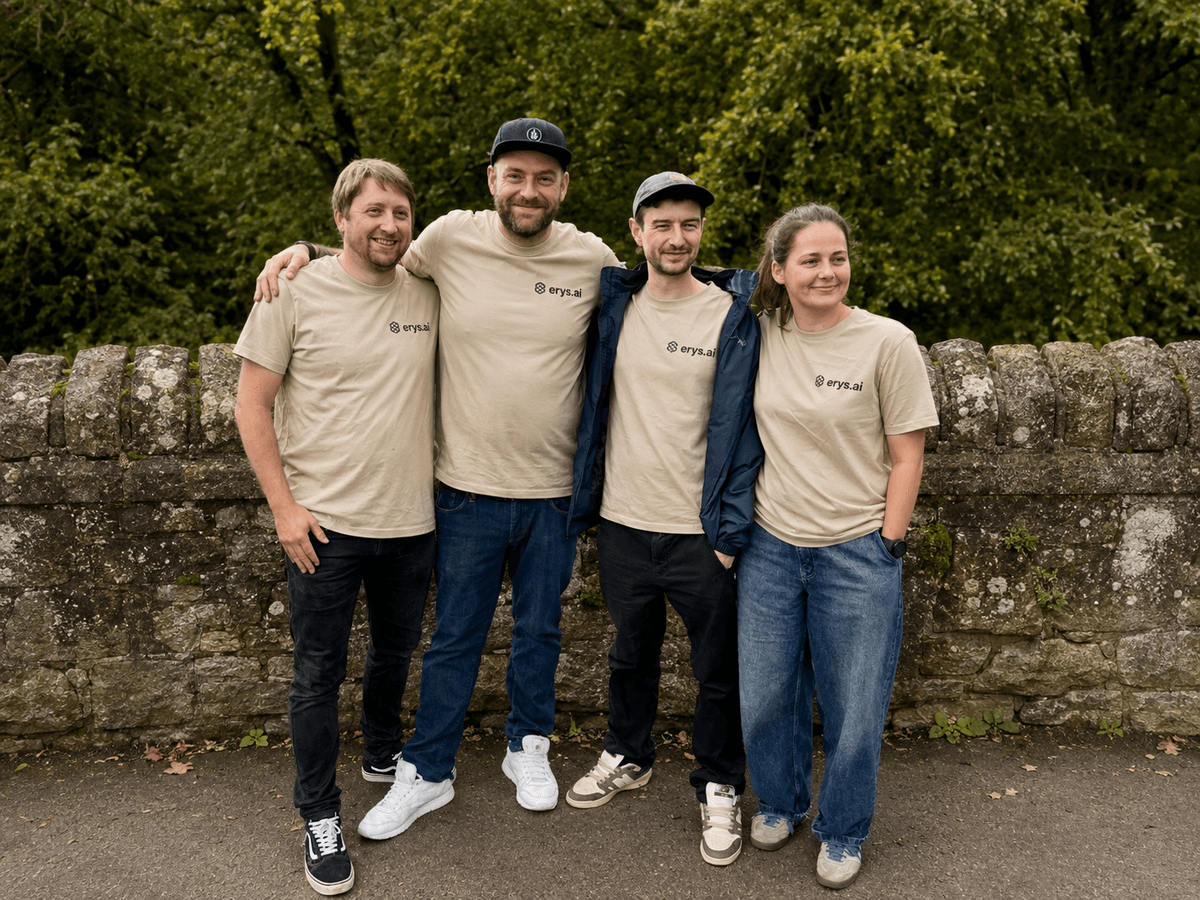 The four person Erys AI team in branded T-shirts, standing against a stone wall